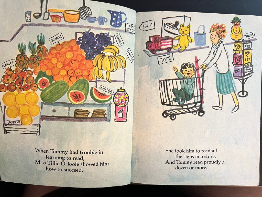 An two page picture book spread. A woman pushes a child in a shopping cart through a grocery story. Many items are labelled with simple signs. The text reads "When Tommy had trouble in learning to read, Miss Tillie O'Toole showed him how to succeed. She took him to read all the signs in a store, And Tommy read proudly a dozen or more."